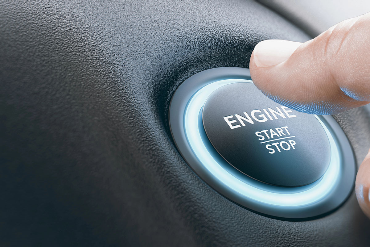 A close-up image of a hand pressing a push-to-start engine button, labeled "ENGINE" with the words "START" and "STOP," illuminated by a soft blue glow.
