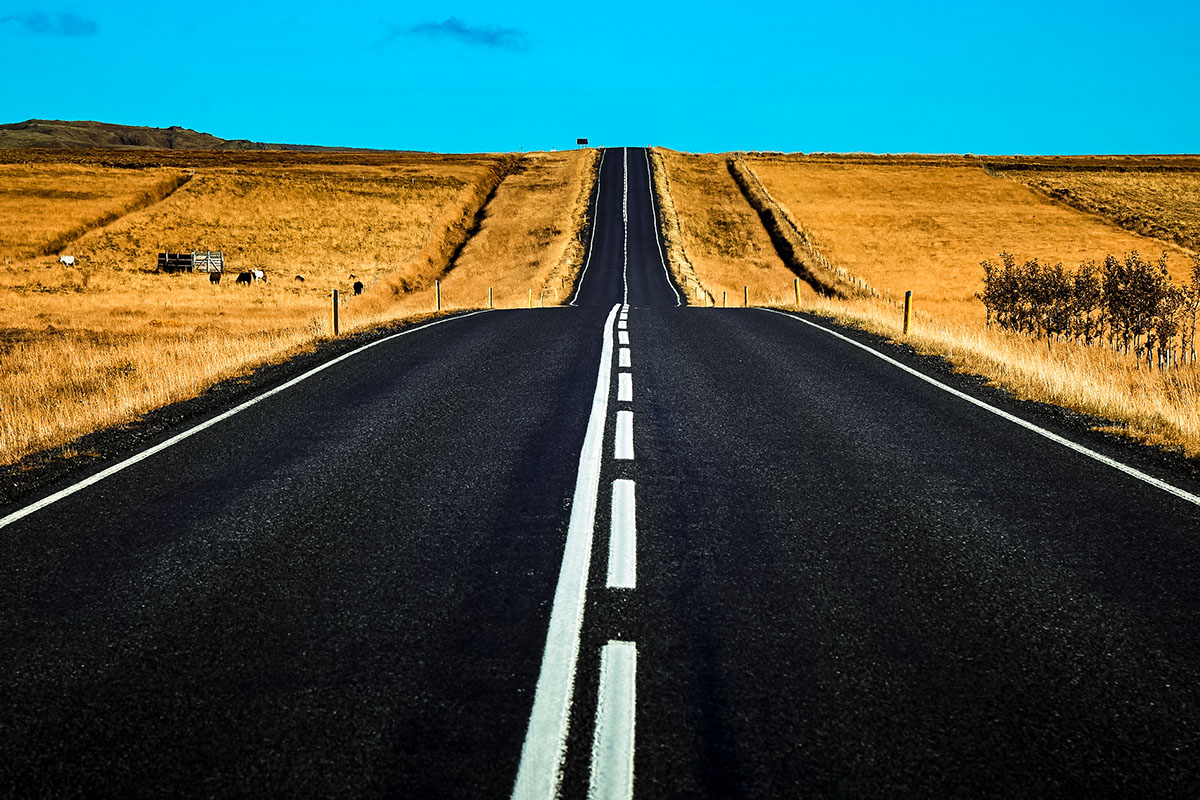 A winding road leads into the distance through golden fields under a clear blue sky.