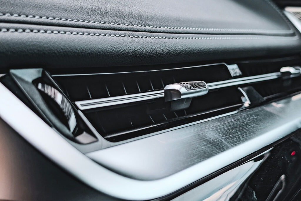 Close-up of a car's dashboard air vent, featuring a sleek design with a metallic adjustment lever and a textured leather surface in the background.
