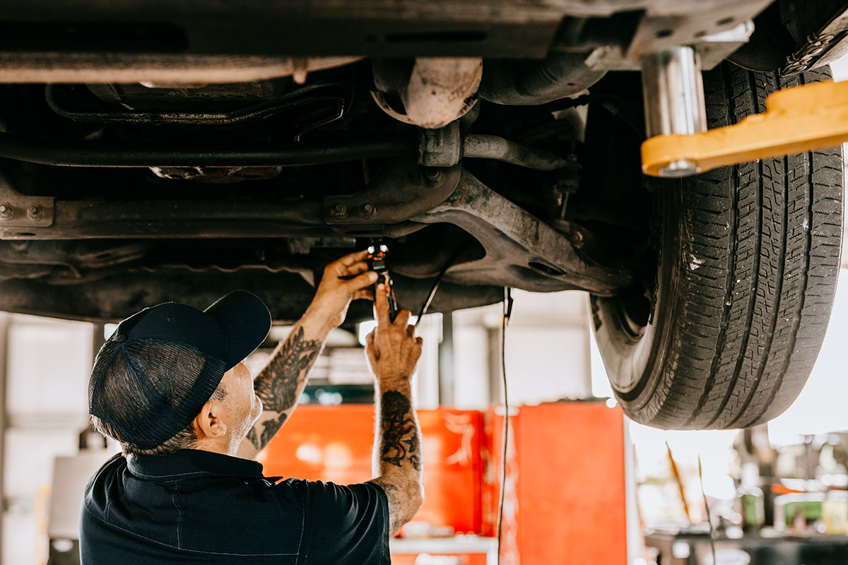 Photoshoot A mechanic with tattoos works under a vehicle, using a wrench to adjust a part while the car is lifted on a hydraulic jack.