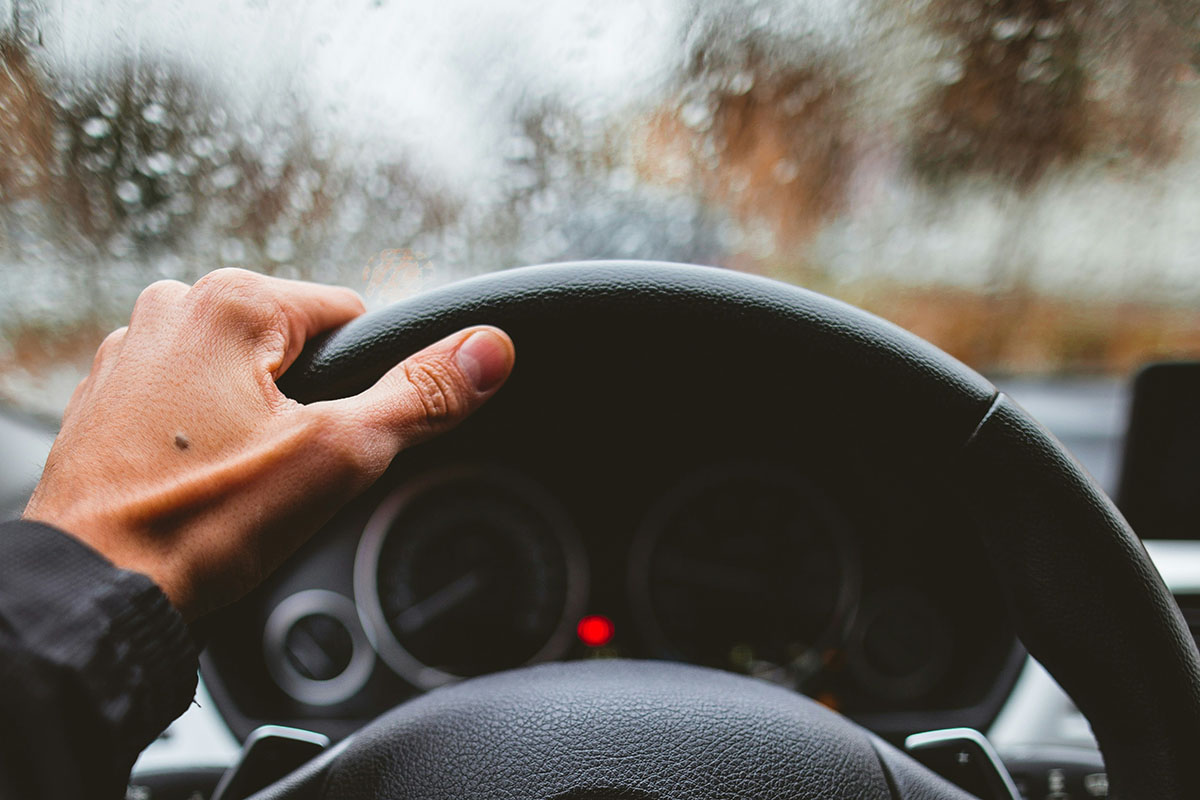 Hand gripping a steering wheel, with a focus on Buda tire alignment and rainy weather.