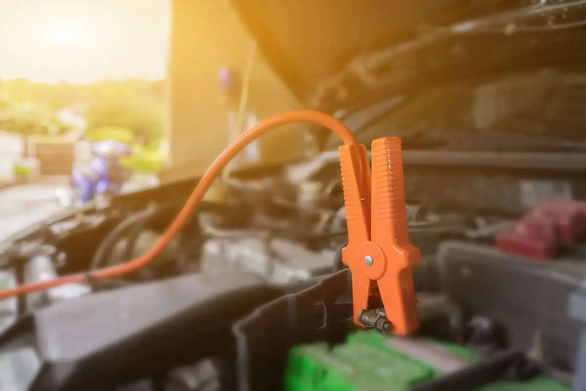 Car battery being tested with a multimeter in sunny weather.