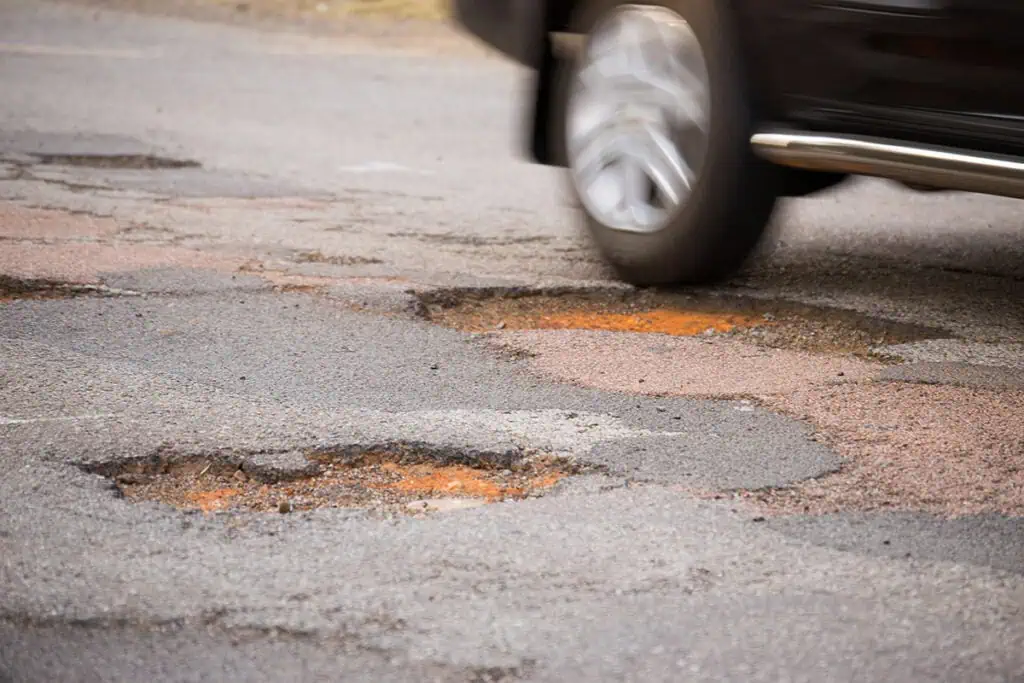 Car driving over potholes on a damaged road surface.