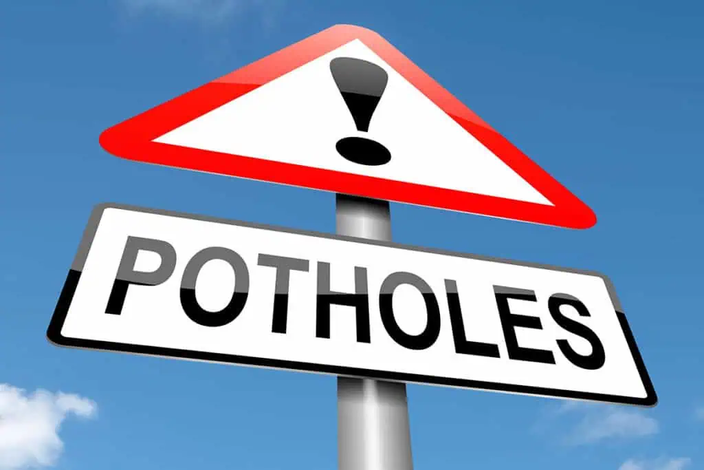 A low-angle view of a traffic sign with a red-bordered triangle containing a black exclamation mark above a white rectangular sign that reads "POTHOLES".